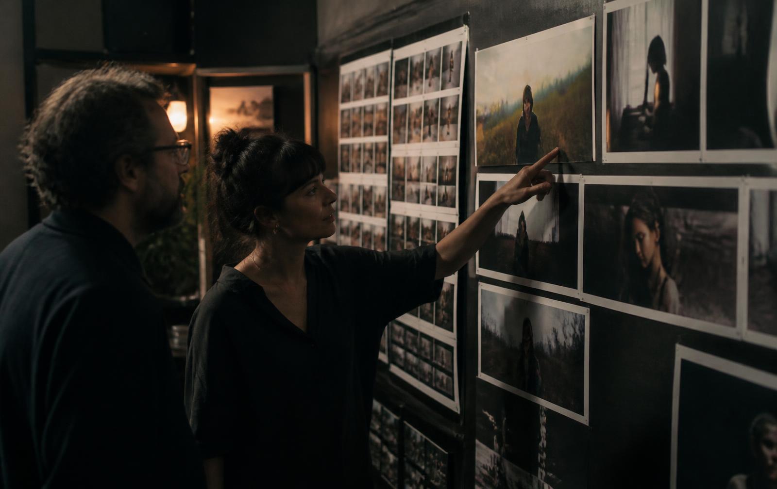 Two people reviewing printed image frames pinned across a studio wall